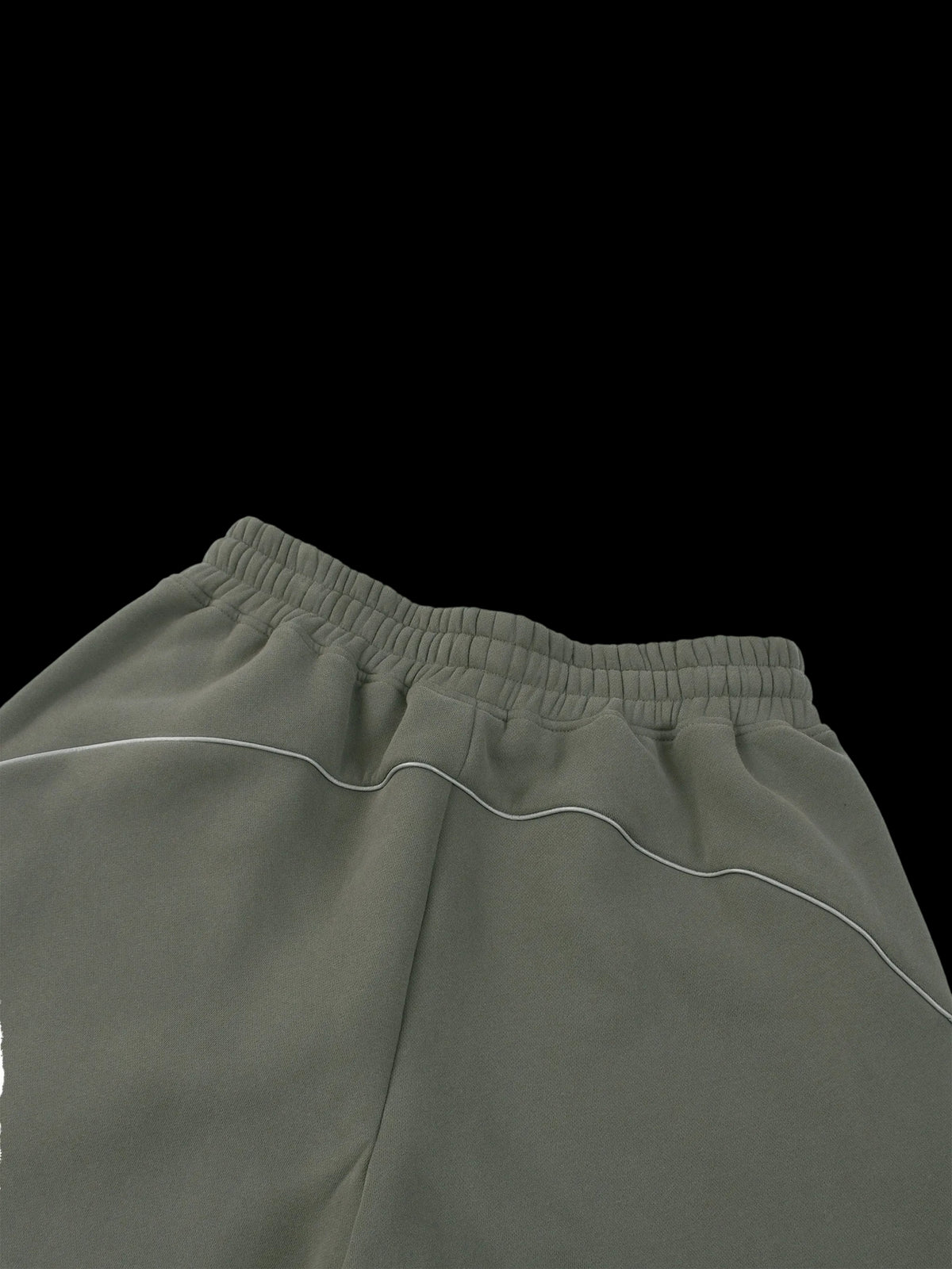 Close-up of the waistband and upper front of olive green sweatpants with thin white contrast piping, shown against a plain white background.