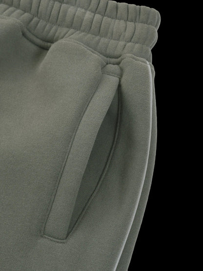 Close-up of olive green sweatpants showing the elastic waistband and a side pocket detail against a white background.