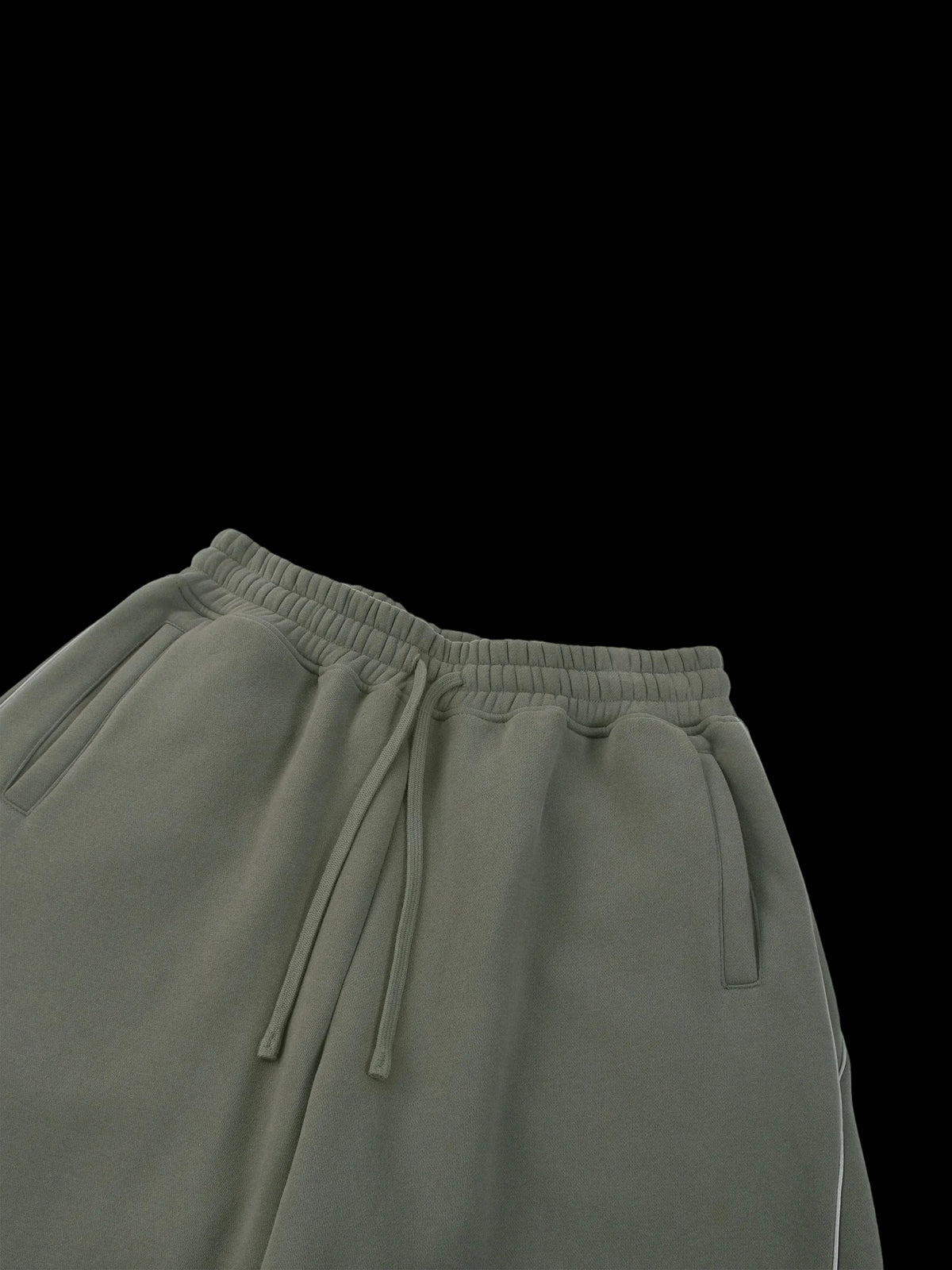 Close-up of the waistband of olive green sweatpants with an elastic drawstring, shown against a plain white background.