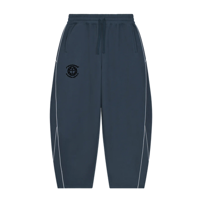 A pair of dark slate blue sweatpants with white side piping and a black circular logo on the left thigh, displayed against a solid white background.