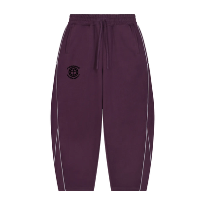 A pair of dark purple jogger-style pants with white piping along the sides and a black circular logo on the left chest, displayed against a solid white background.