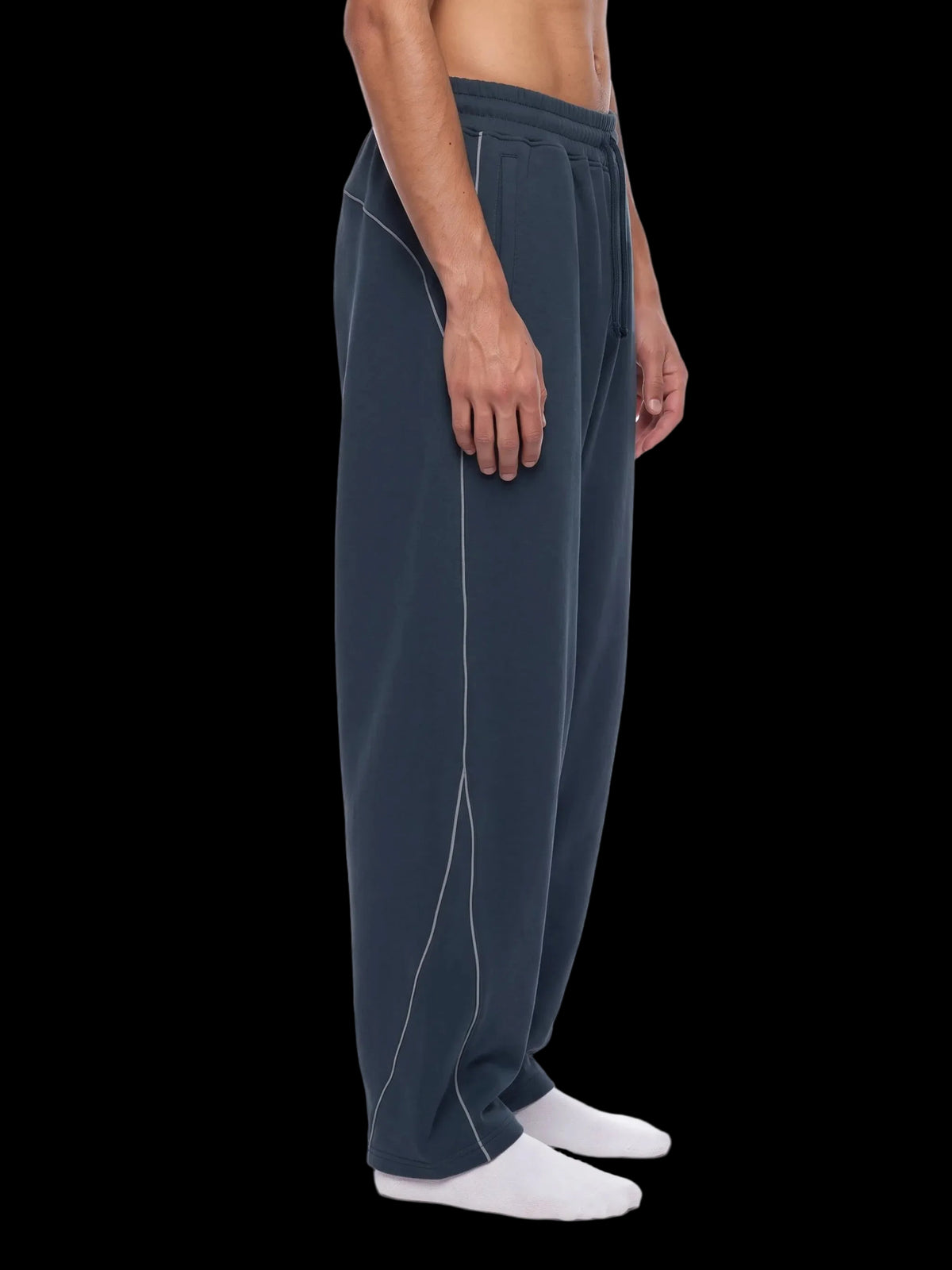 A side profile view of a person wearing dark slate blue sweatpants with white contrast stitching, paired with white socks, against a plain white background.