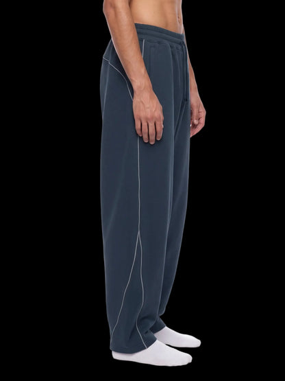 A side profile view of a person wearing dark slate blue sweatpants with white contrast stitching, paired with white socks, against a plain white background.